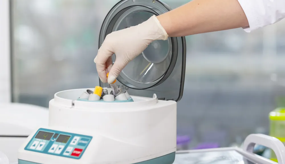 A gloved hand placing a tube into a centrifuge